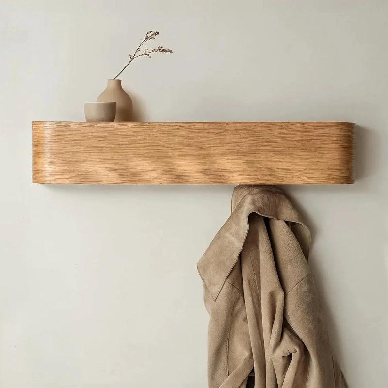 Wood & Iron Coat Rack with Hidden Hooks & Shelf mounted on a pale wall; beige coat hangs with a small vase on the shelf.
