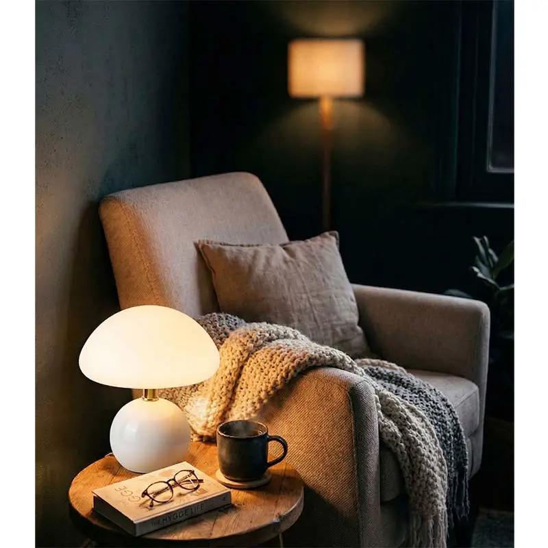 Nordic Ceramic Mushroom Table Lamp, white, on a round wooden side table beside a cosy armchair in a living room.