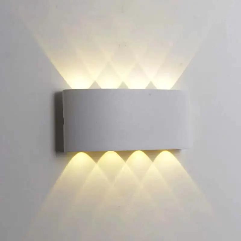 A modern rectangular wall sconce light fixture mounted on a white wall, casting warm light upward and downward in a diamond pattern.