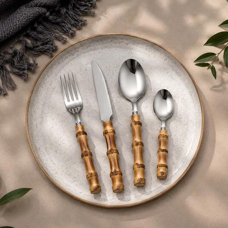 24-Piece Bamboo Handle Cutlery Set on a speckled ceramic plate; four bamboo-handled stainless steel utensils.