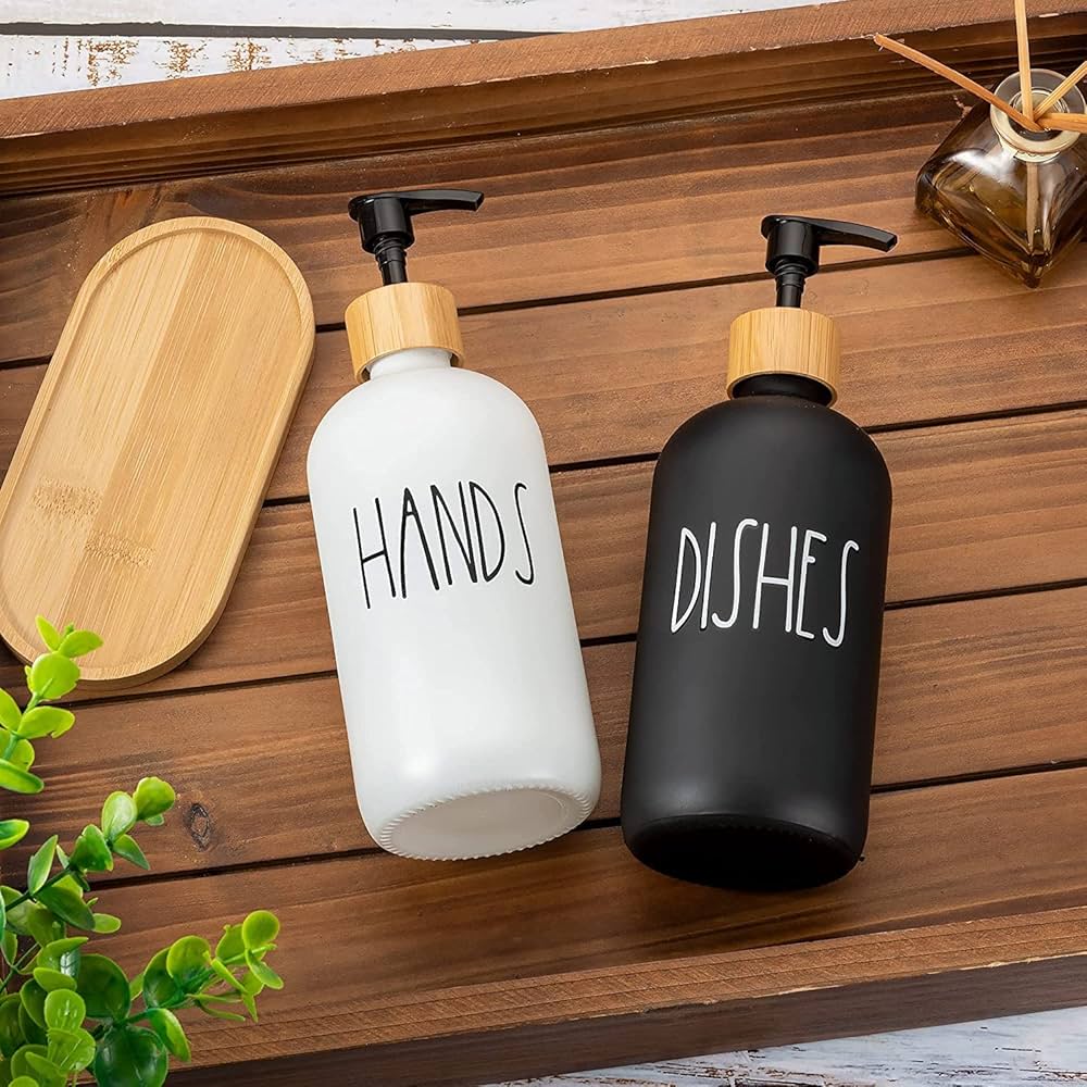 Two soap dispensers labeled 'HANDS' and 'DISHES' on a wooden surface with a wooden tray and plant in the background.