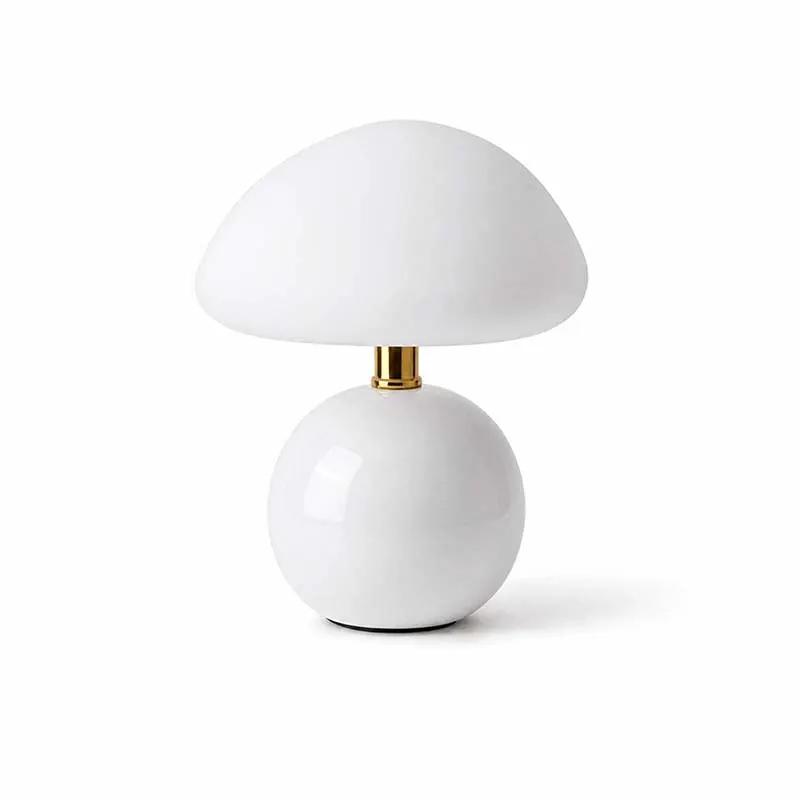 A mushroom-shaped table lamp with a glossy white ceramic base and a matte white dome-shaped shade, accented by a small gold metal neck, set against a plain white background.