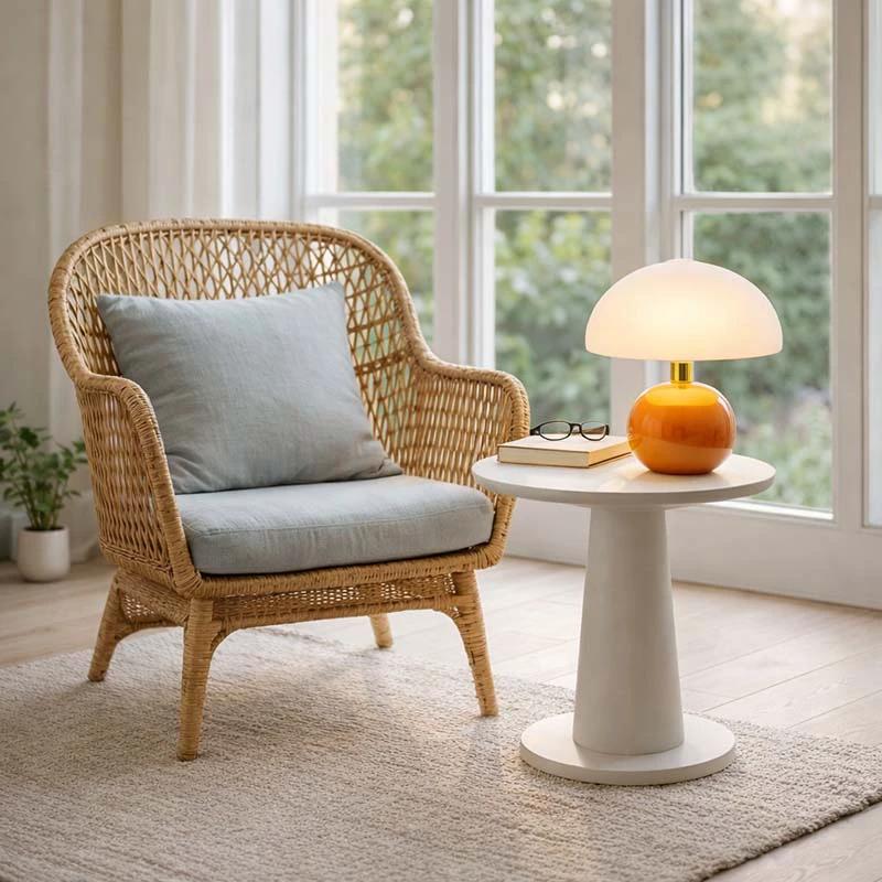 Nordic Ceramic Mushroom Table Lamp with orange base and white shade on a round table beside wicker chair in living room.