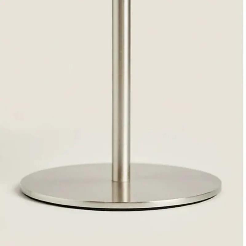 Close-up of a brushed metal stand base with a vertical pole on a light beige background.