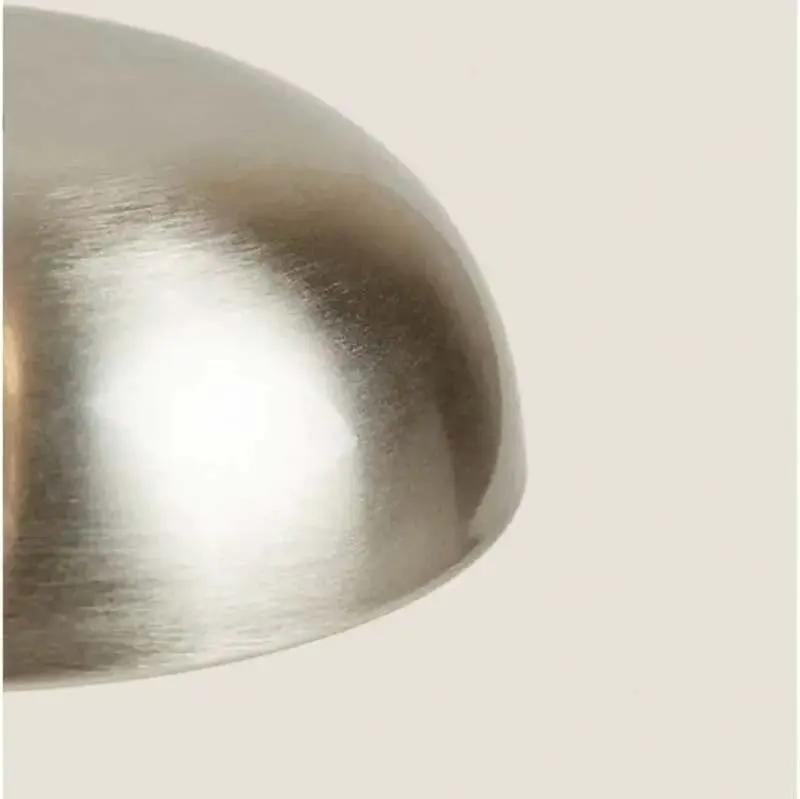 Close-up of a brushed metal dome-shaped object, likely a lamp shade or decorative dome, on a plain light beige background.