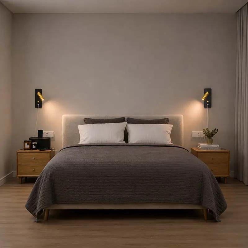 A modern bedroom scene featuring a bed dressed in a textured dark gray quilt and white pillows, flanked by two matching wooden nightstands and black wall sconces against a warm gray wall.