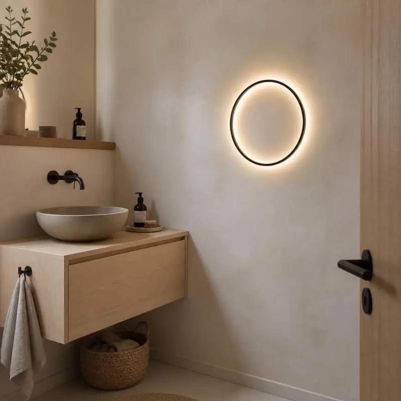 A modern minimalist bathroom scene featuring a floating light wood vanity with a stone vessel sink, a black wall-mounted faucet, and a glowing circular black LED wall light on the beige plaster wall.